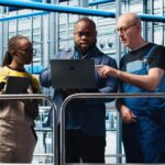 A consultant, engineer, and technician collaborate with a laptop on an industrial factory floor to define an MVP strategy.