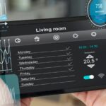A multi-ethnic team of engineers on a factory floor reviews transparent holographic data visualizations and dashboards on a laptop, demonstrating the predictive monitoring required for Scaling IoT infrastructure.