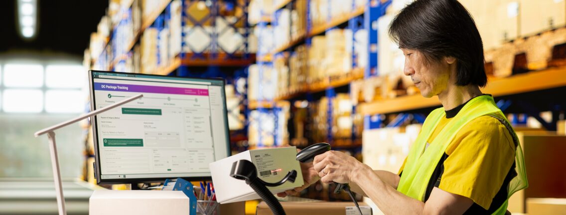 A warehouse worker in a yellow vest scans a package while sophisticated holographic data overlays visualize a new modern supply chain platform, featuring Docker containers, Kubernetes clusters, and 99.95% uptime enabled by Wishtree.